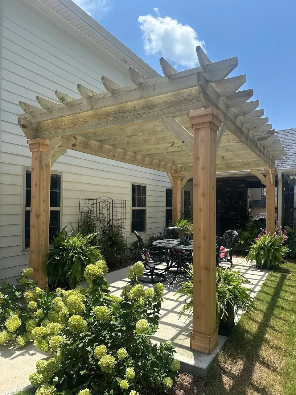 A custom cedar pergola over an at-grade paver patio with outdoor dining and hydrangeas at a Newnan, GA home by QWR